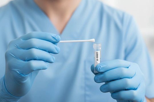 Врач держит в руках пробирку с надписью covid-19 и ватную палочку
