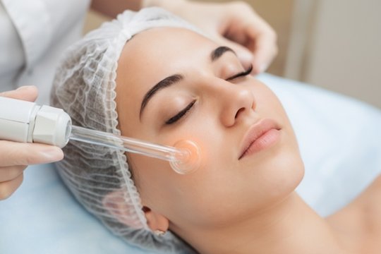 Врач проводит пациенту процедуру дарсонвализации лица и кожи головы на дому